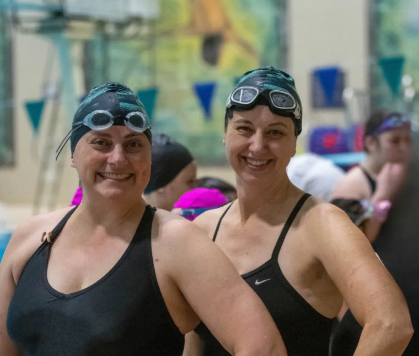 Two Masters swimmers in caps and goggles, smiling at the side of the pool.