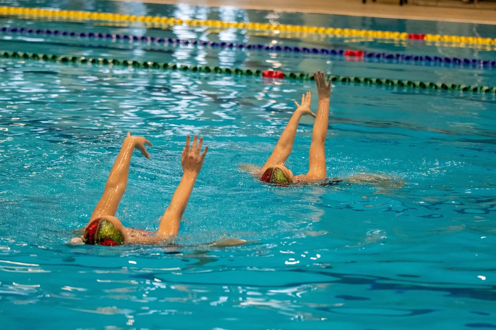 Two swimmers lifting their arms out of the water in unison.