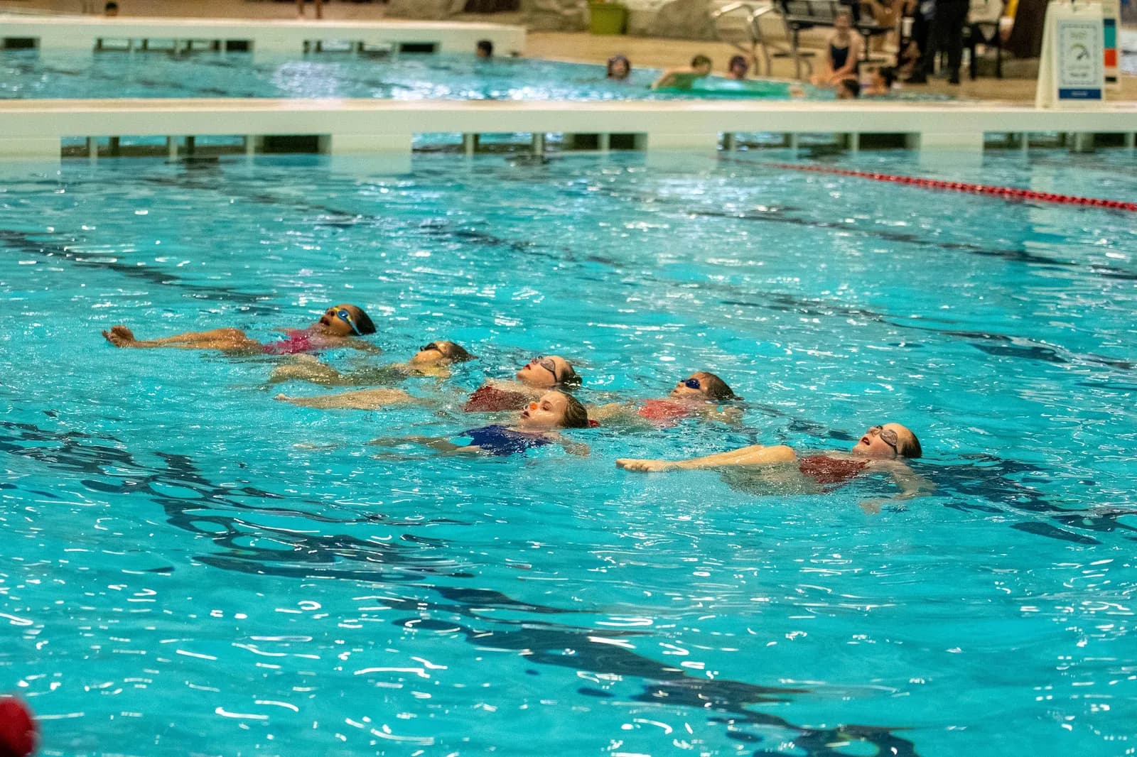 Young swimmers holding a back layout in a line across the pool.